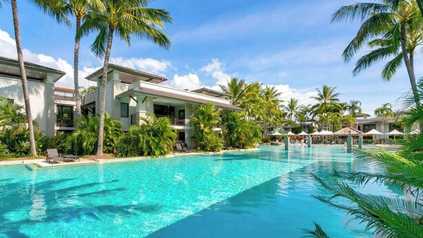A resort with a large swimming pool, palm trees, and modern buildings. - Poolside Bliss: A Modern Resort Sanctuary (Port Douglas)