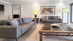 A modern living room with two sofas, a coffee table, a lamp, and a framed artwork on the wall. - Poolside Bliss: A Modern Resort Sanctuary (Port Douglas)