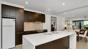 A modern kitchen with dark wood cabinets, a white island, and a tiled backsplash. - Poolside Bliss: A Modern Resort Sanctuary (Port Douglas)