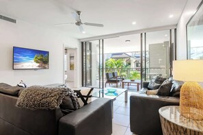 A modern living room with a flat-screen TV, two sofas, a coffee table, and a balcony with outdoor furniture.