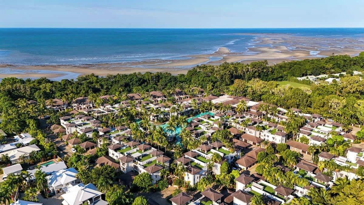 Un quartier résidentiel en bord de mer, avec des maisons, une piscine et une plage en arrière-plan.