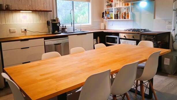 Une cuisine moderne avec une table à manger en bois et des chaises blanches, équipée d’un lave-vaisselle, d’un four à micro-ondes et d’une cuisinière à gaz.