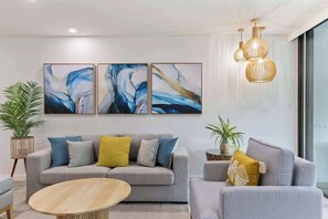 A modern living room with a grey sofa, a round wooden coffee table, and abstract paintings on the wall.