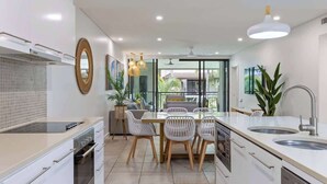 A modern kitchen with white cabinetry, a dining area with white chairs, a large window, and a view of the outside. - Rooftop Resort Oasis at Temple with Spa (Craiglie)