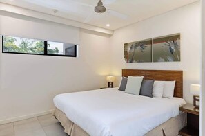 A bedroom with a bed, a ceiling fan, a nightstand, a wall-mounted TV, and a painting.