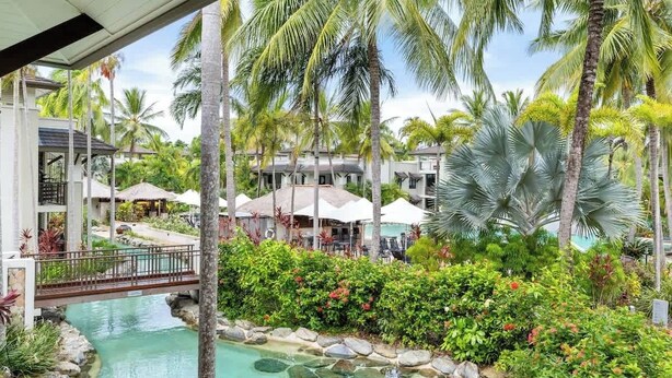 A resort with a swimming pool, palm trees, and a bridge. - Devine Rooftop Penthouse at Temple Resort (Port Douglas)