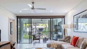 A modern living room with a sofa, coffee table, and TV stand. There is a balcony with outdoor furniture. - Devine Rooftop Penthouse at Temple Resort (Port Douglas)
