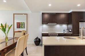 A modern kitchen with dark cabinetry, a tiled backsplash, and a central island with a sink.