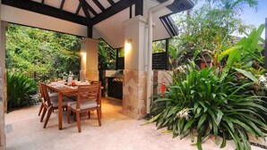 An outdoor patio with a stone barbecue, wooden dining table, and chairs. - The Villa at Temple: A Luxury Resort Hideaway (Port Douglas)