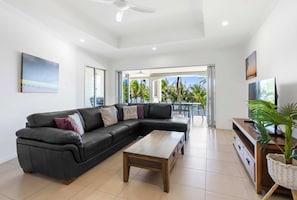 A modern living room with a sectional sofa, a coffee table, and a TV stand. - Verde at Island Views—Palm Cove Waterfront Bliss (Palm Cove)