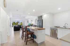 A modern kitchen with a central island, a built-in dishwasher, and a dining area with a sofa and chairs. - Verde at Island Views—Palm Cove Waterfront Bliss (Palm Cove)