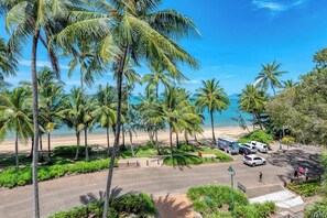 A beachside view with palm trees, a parking area, and a clear blue sky.
