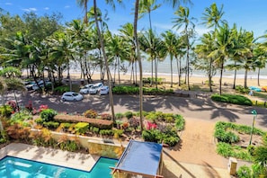 A resort with a swimming pool, a parking area with cars, and a beach with palm trees. - Verde at Island Views—Palm Cove Waterfront Bliss (Palm Cove)