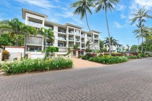 Un hotel a più piani con balconi, immerso nel verde di palme e giardini curati.