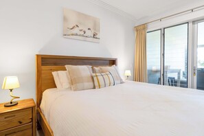A hotel room with a large bed, a nightstand with a lamp, a painting on the wall, and a sliding glass door to the balcony. - Verde at Island Views—Palm Cove Waterfront Bliss (Palm Cove)