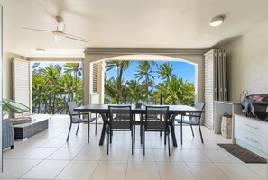 A modern dining area with a table and chairs, a ceiling fan, and a view of palm trees. - Verde at Island Views—Palm Cove Waterfront Bliss (Palm Cove)