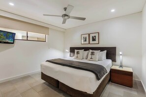 A bedroom with a bed, nightstand, ceiling fan, wall-mounted TV, and framed pictures. - Paradise Bound: A Rooftop Resort Retreat (Palm Cove)