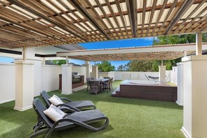 A covered outdoor patio with artificial grass, lounge chairs, a barbecue grill, and a hot tub. - Paradise Bound: A Rooftop Resort Retreat (Palm Cove)