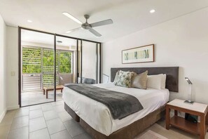 A bedroom with a bed, a nightstand, a ceiling fan, and a sliding glass door leading to a balcony.