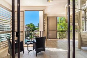 A balcony with a wicker chair, a small round table, and a view of a swimming pool and trees.