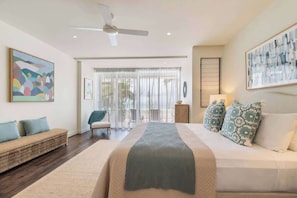 A modern bedroom with a large bed, a sofa, a ceiling fan, and artwork on the walls.