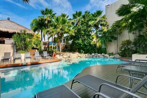 Ein Pool mit Liegestühlen, Palmen und einer Struktur mit Reetdach.