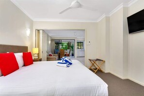 A hotel room with a bed, a TV, a ceiling fan, and a view of the outside.