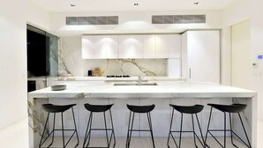 A modern kitchen with a marble countertop, black bar stools, and white cabinets.
