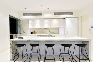 Una cucina moderna con un piano di lavoro in marmo, sgabelli da bar neri e mobili bianchi.