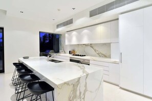 A modern kitchen with a marble countertop, black bar stools, and white cabinetry.