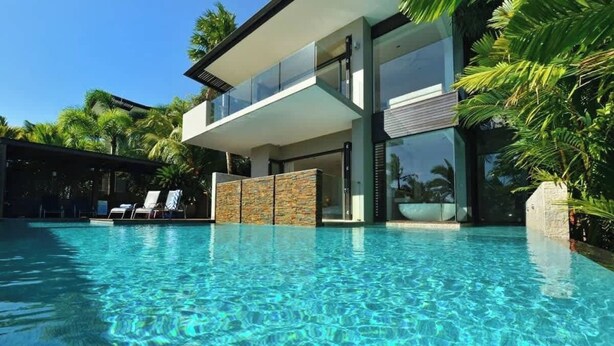 A modern house with a swimming pool, glass balustrades, and a stone facade.