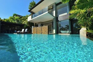 Una casa moderna con piscina, barandillas de vidrio y fachada de piedra.