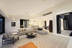 A modern living room with a sectional sofa, a coffee table, and a dining area in the background.