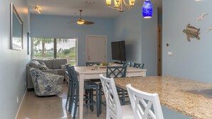 A modern kitchen with a granite countertop, a dining table with blue chairs, and a ceiling fan. - Casual Condo Near Beach w/ Pools, hot tub & Grill! (South Padre Island)