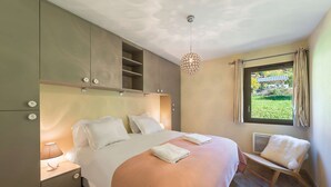 A bedroom with a bed, bedside tables, a hanging light fixture, a window with curtains, and a view of greenery outside. - Les 4 ELEMENTS - A11 (CHATEL)