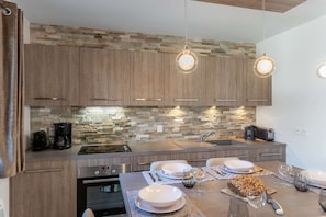 A modern kitchen with a stone backsplash, wooden cabinets, and pendant lighting.