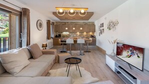 A modern living room with a sofa, a TV, and a kitchen in the background. - Les 4 ELEMENTS - A11 (CHATEL)