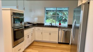 A modern kitchen with white cabinetry, stainless steel appliances, and a window with a view of greenery. - Water view (Mill Valley)