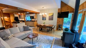 A modern living room with a sofa, coffee table, and fireplace. A dining area with a table and chairs is visible in the background. - 43TV peaceful retreat in the White Mountain, fireplace, fire pit, large yard, WiFi, AC! (Twin Mountain)