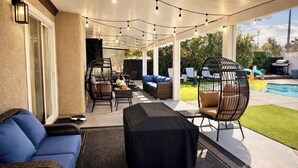 An outdoor patio area with wicker furniture, string lights, and a pool in the background. - ESCAPE THE MADNESS with no better place to relax!  NEW LUXURY SPA AND HUGE POOL! (North Las Vegas)
