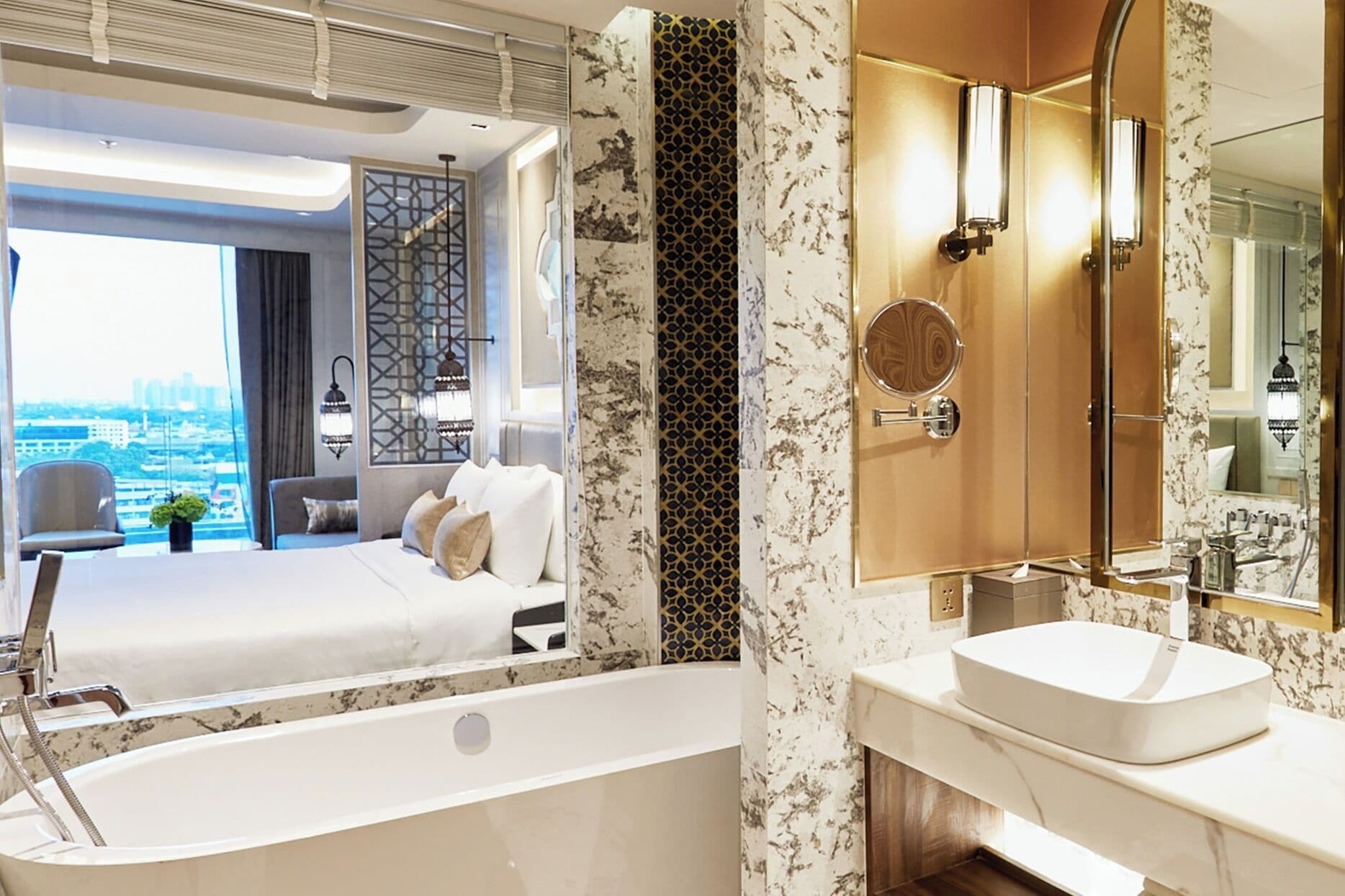 A modern hotel room with a large bed, a sitting area, a bathroom with a bathtub, and a city view.
