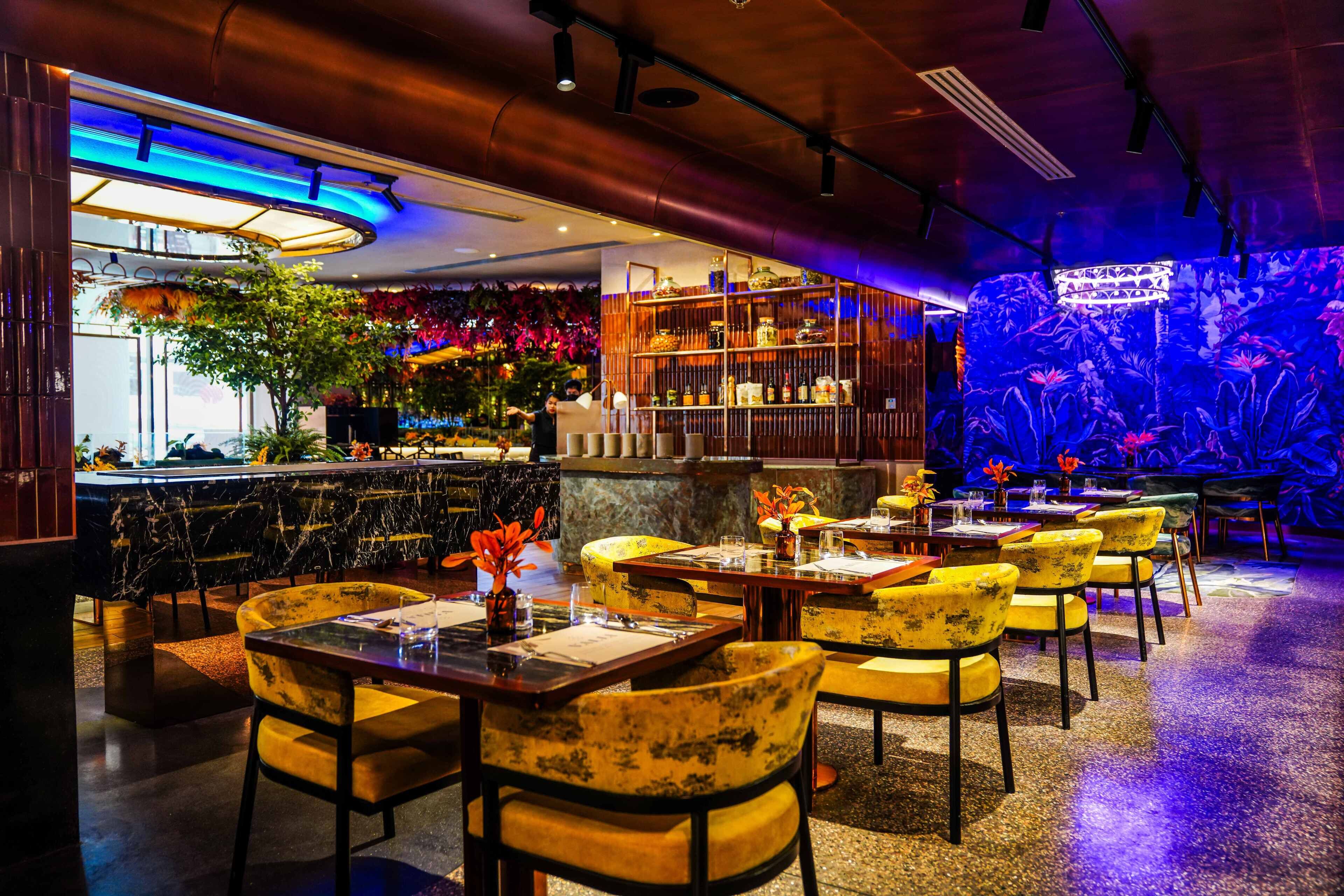 A restaurant with marble bar counters, yellow upholstered chairs, and a blue-lit aquarium wall.
