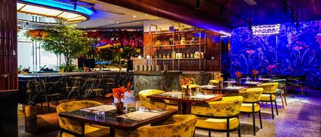 A restaurant with marble bar counters, yellow upholstered chairs, and a blue-lit aquarium wall.