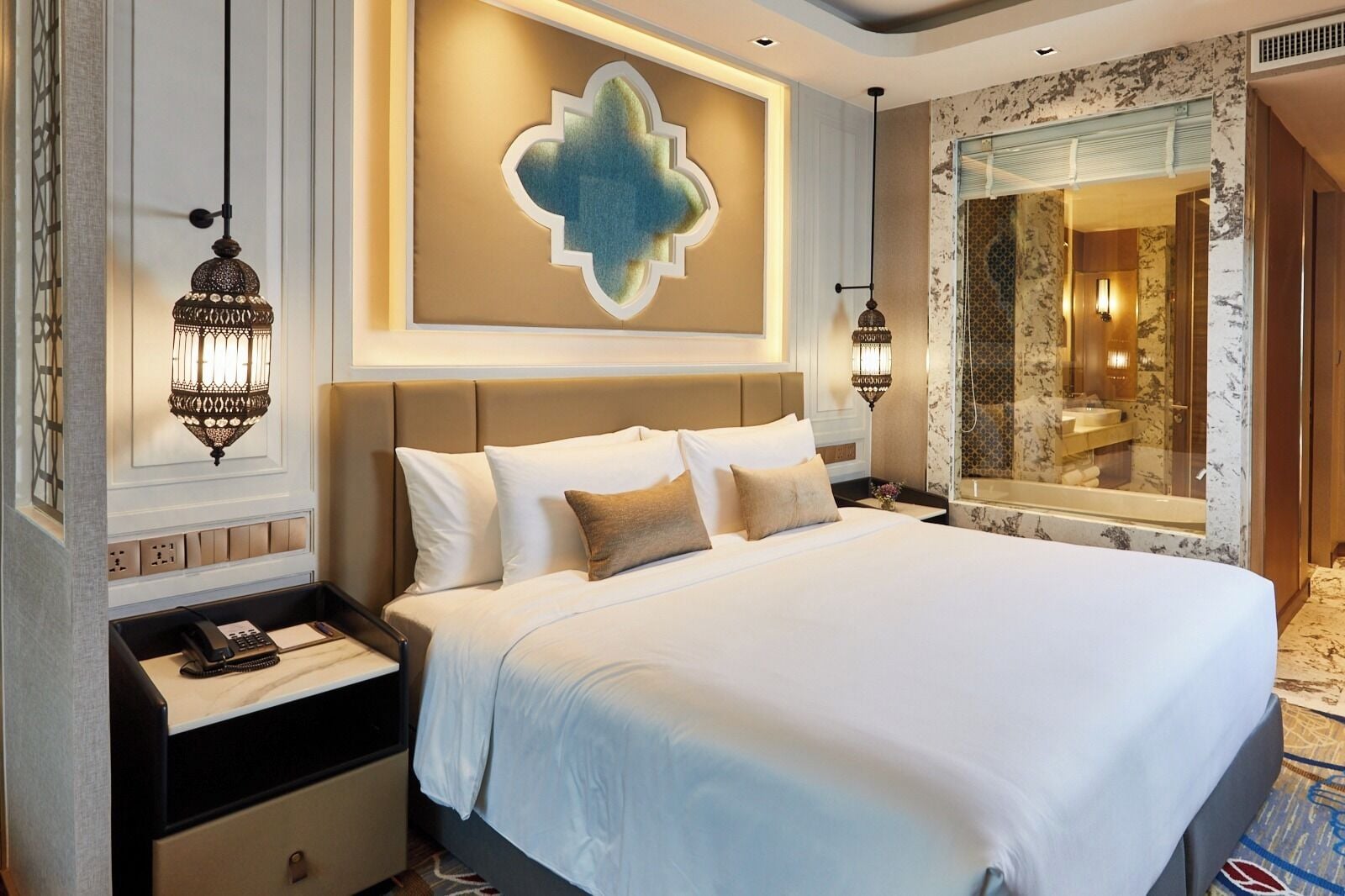 Ein Hotelzimmer mit einem großen Bett, einem Nachttisch mit Telefon und einer wandmontierten Lampe.