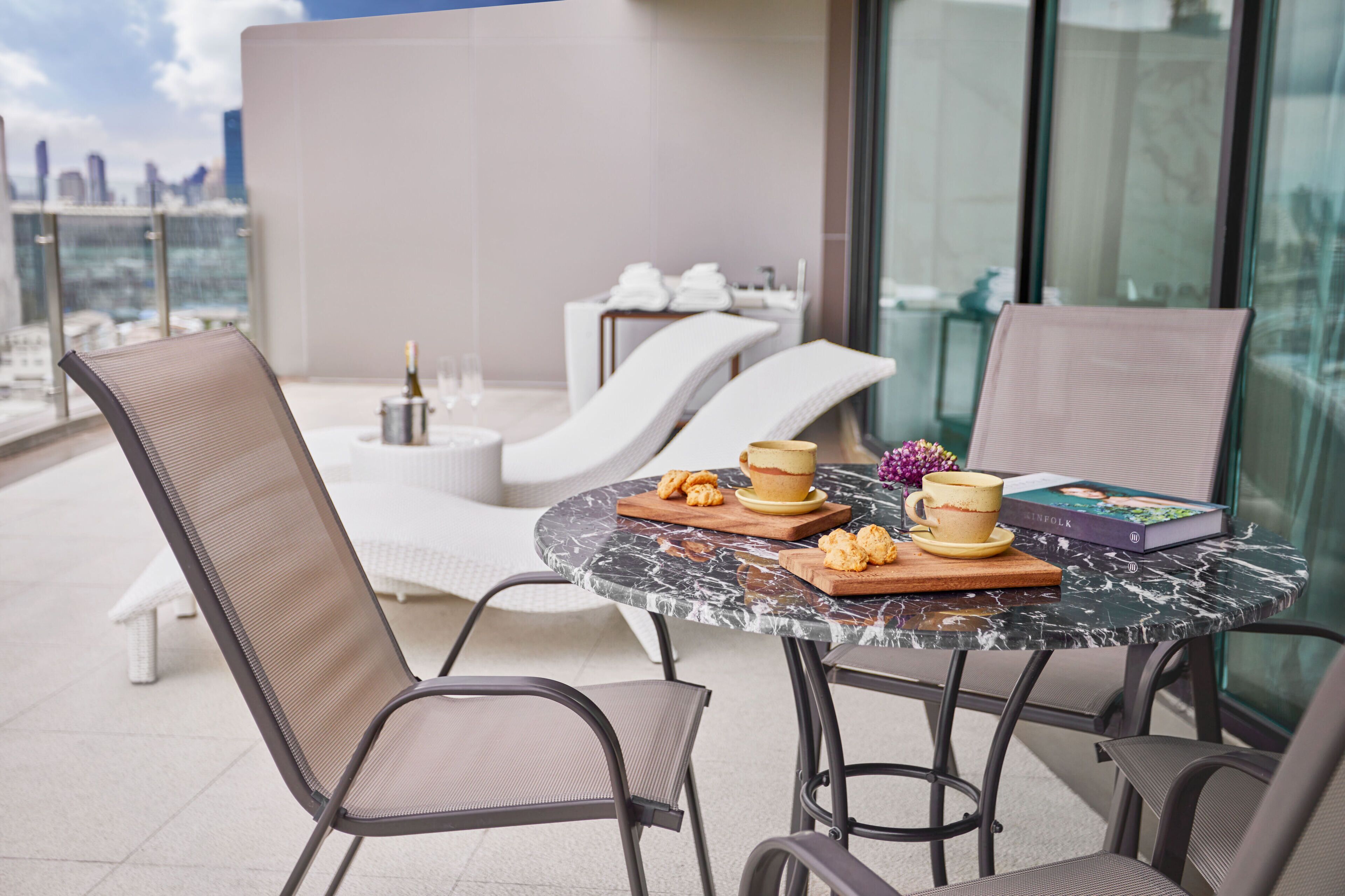 A modern outdoor seating area with a round marble table, cushioned chairs, and a city view.