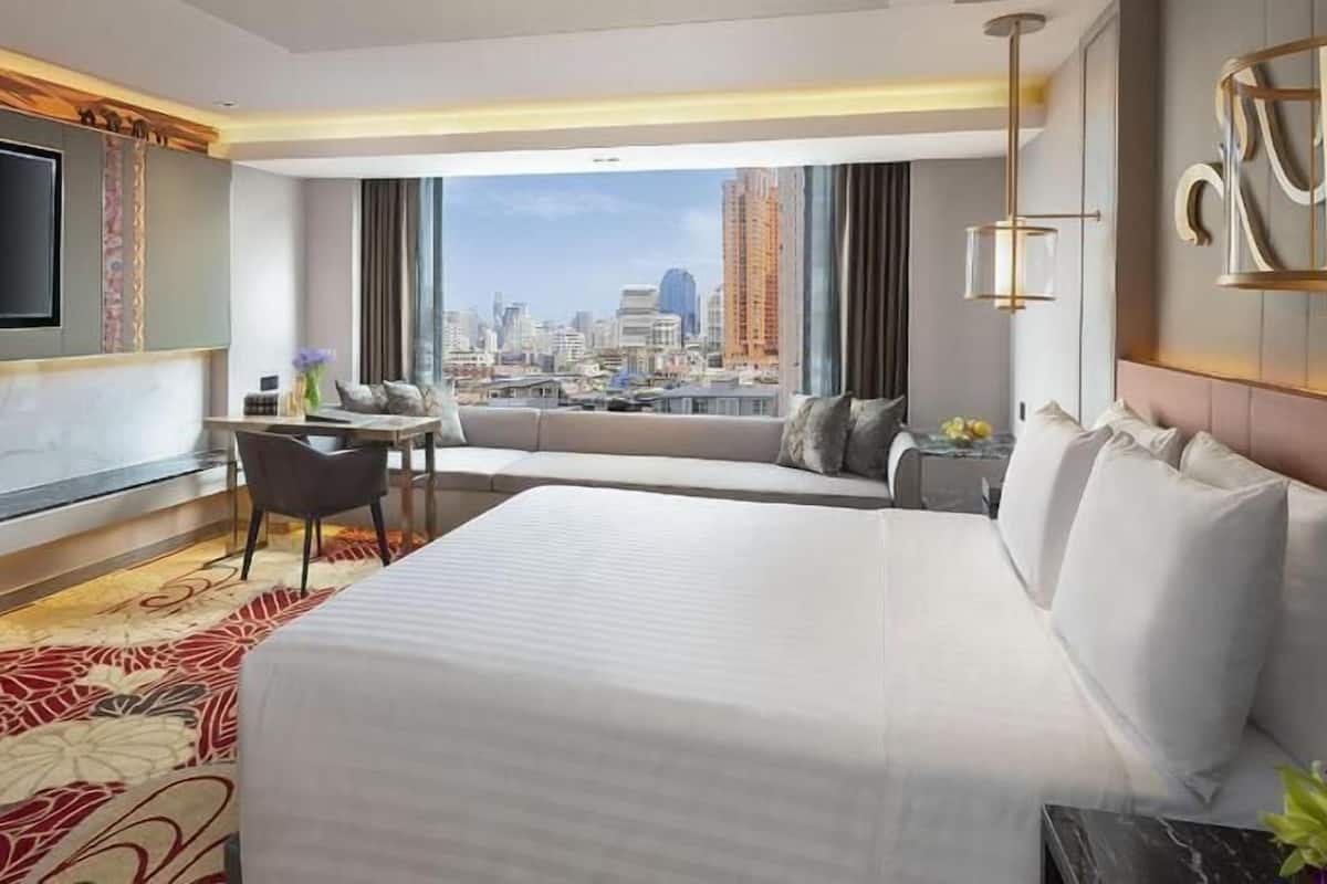 Habitació d'hotel amb un llit gran, televisió, escriptori amb cadira i vista a un paisatge urbà.