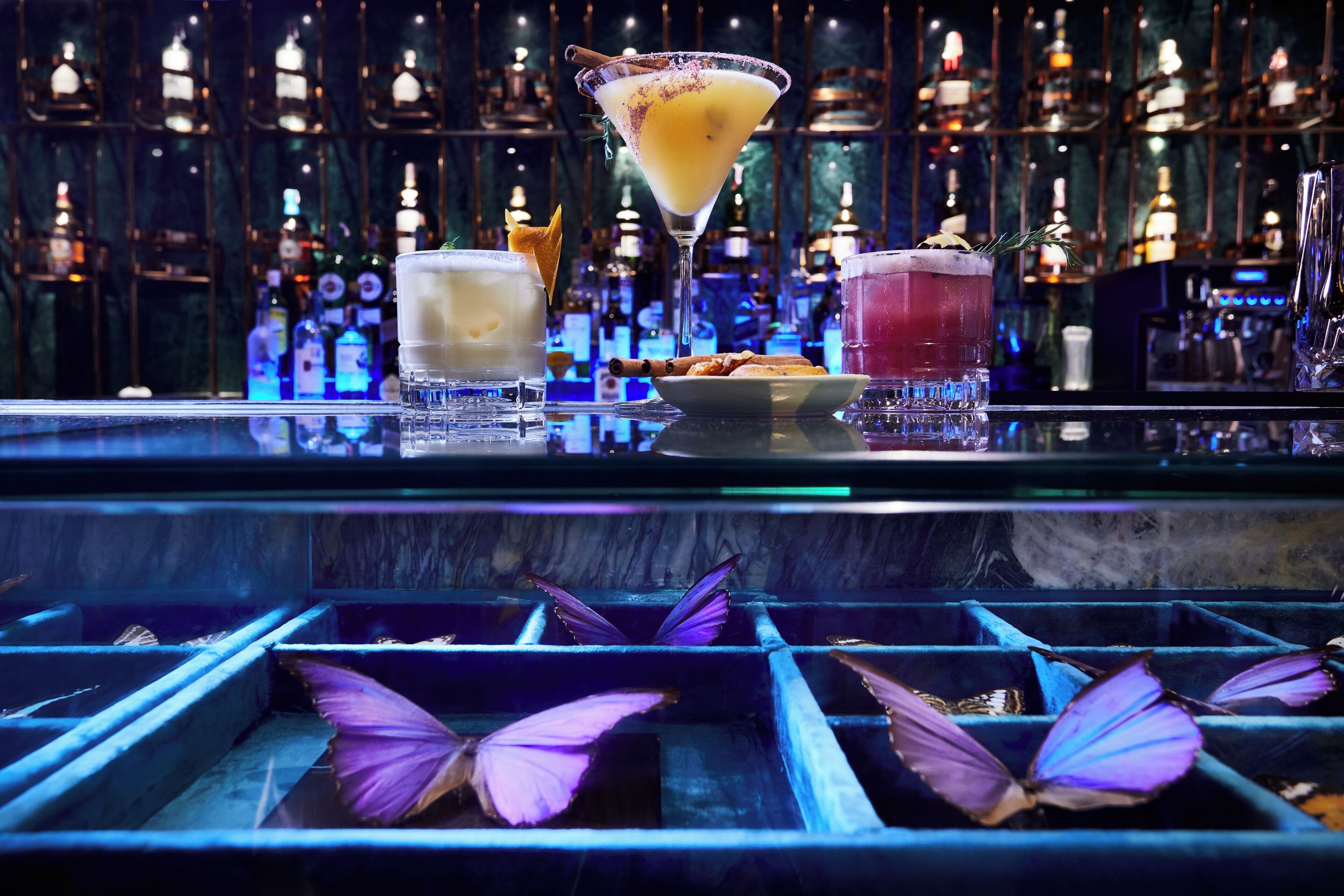 A bar with various cocktails, a plate of snacks, and butterfly decorations.