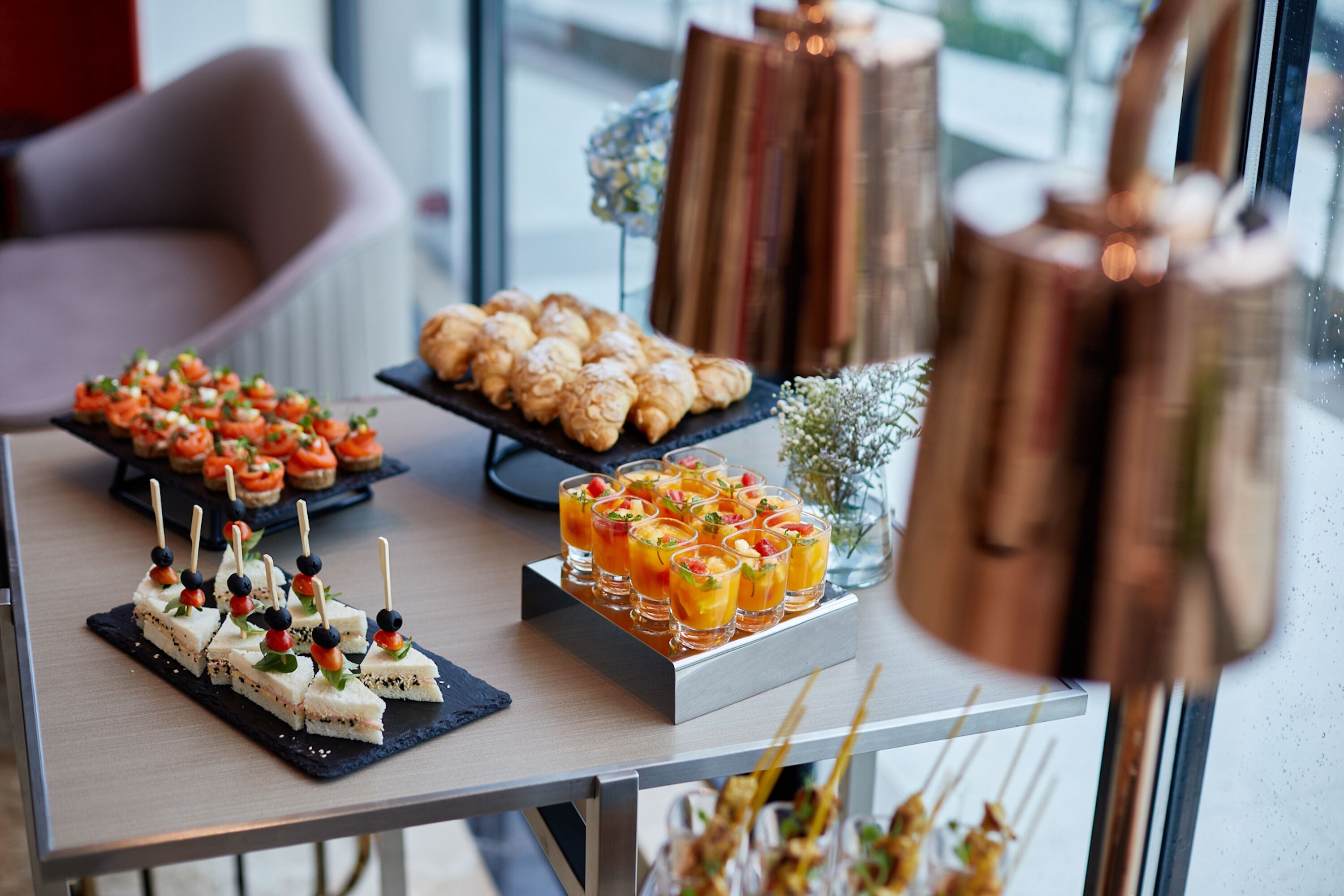 Una mesa de buffet con diversos alimentos, entre ellos aperitivos, pasteles y bebidas.