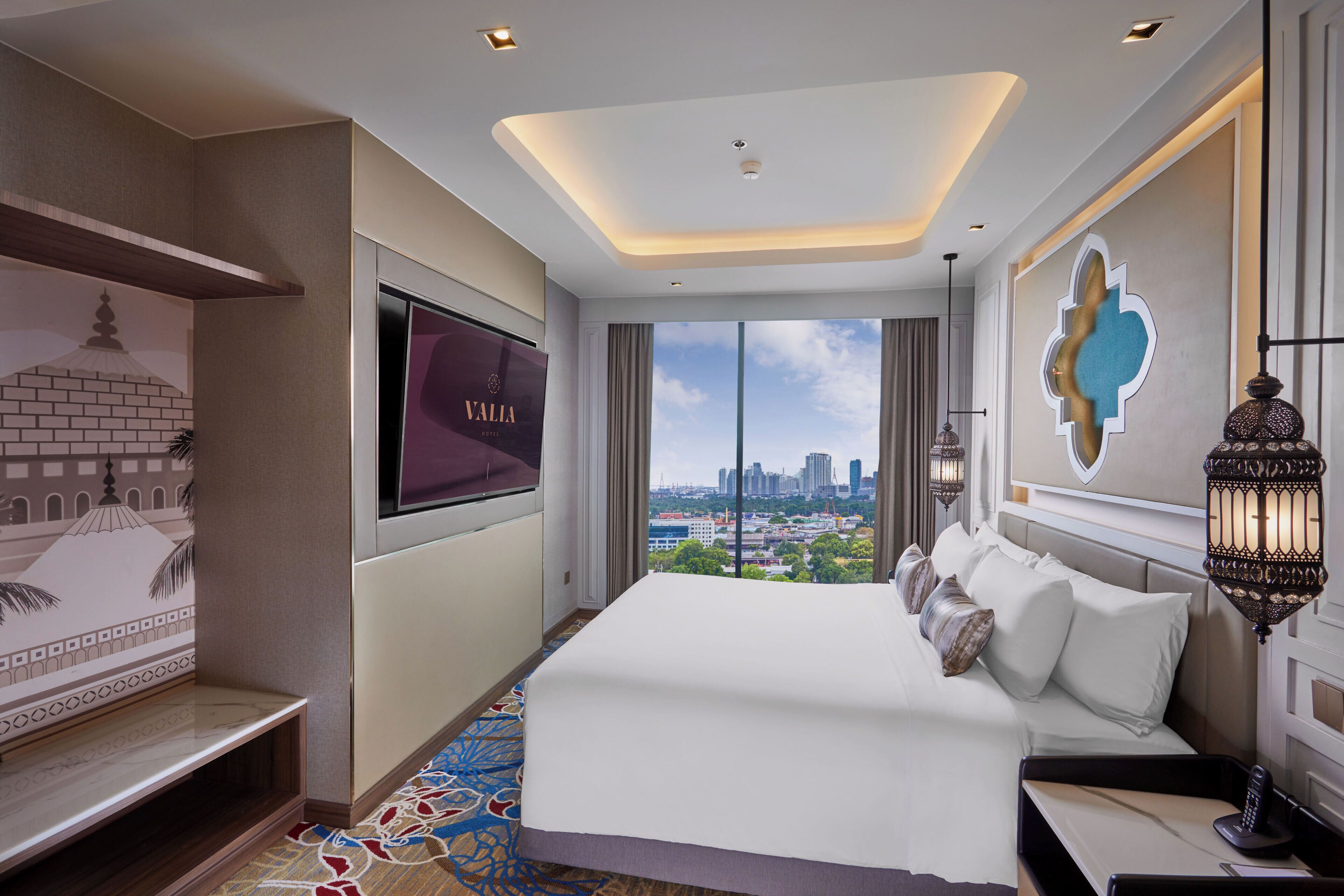 A hotel room with a large bed, a TV mounted on the wall, a city view, and a decorative wall piece.