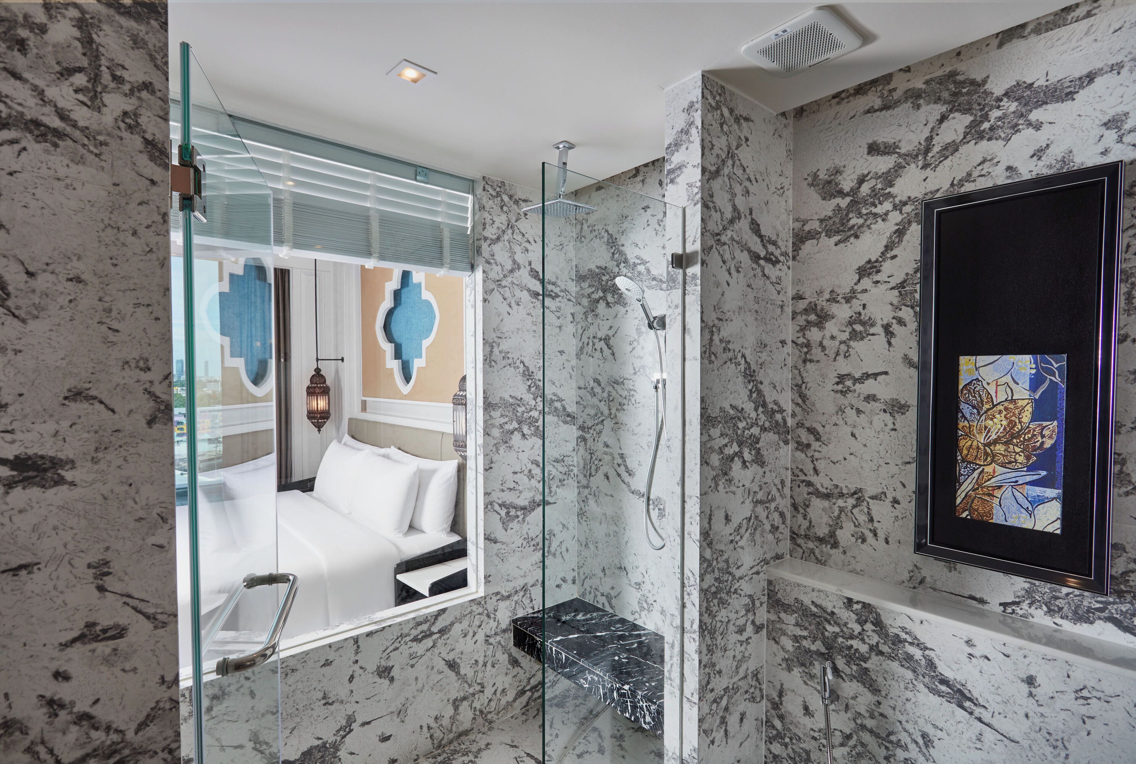 Un baño moderno con cabina de ducha de vidrio, paredes de mármol y una obra de arte enmarcada.